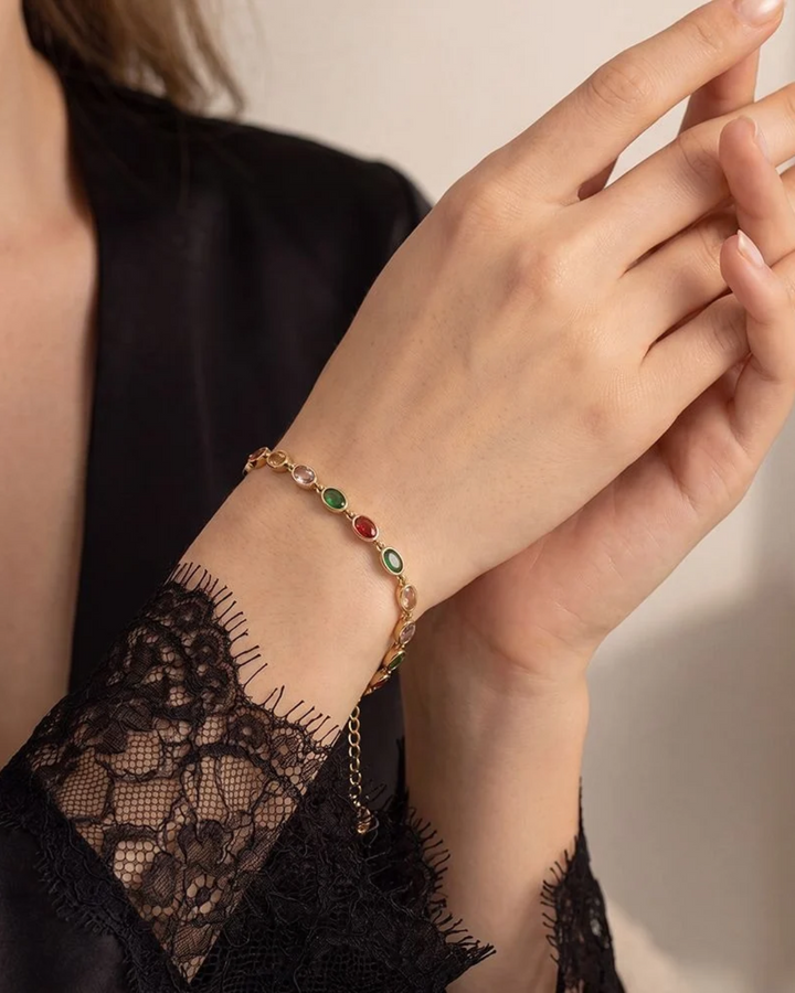 Armband mit bunten Steinen von Dottilove getragen von einer Frau mit schwarzen Oberteil. Das Armband selbst ist gold mit bunten Steinen in grün, rot lila und gelb.