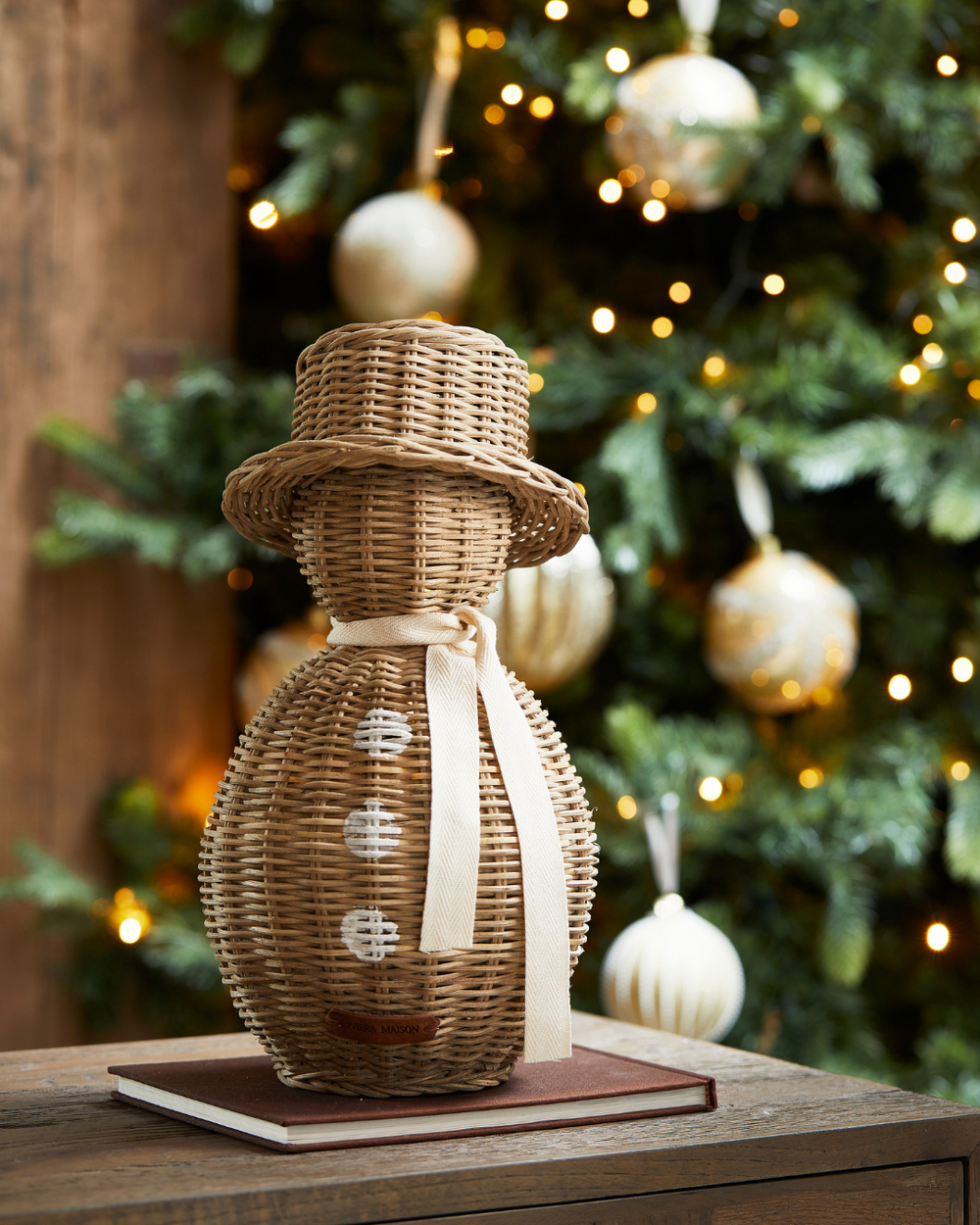 Großer Rustic Rattan Schneemann von Rivièra Maison vor einem Weihnachtsbaum auf einem Holztisch mit Buch dekoriert.