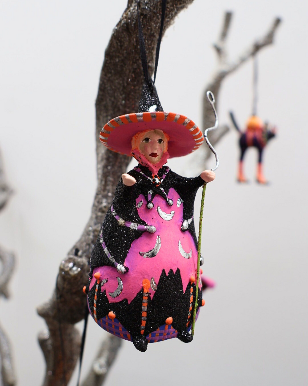 Der Hexen Krinkle Mini Bat Moon Witch von Patience Brewster hängt an einem knorrigen Ast.