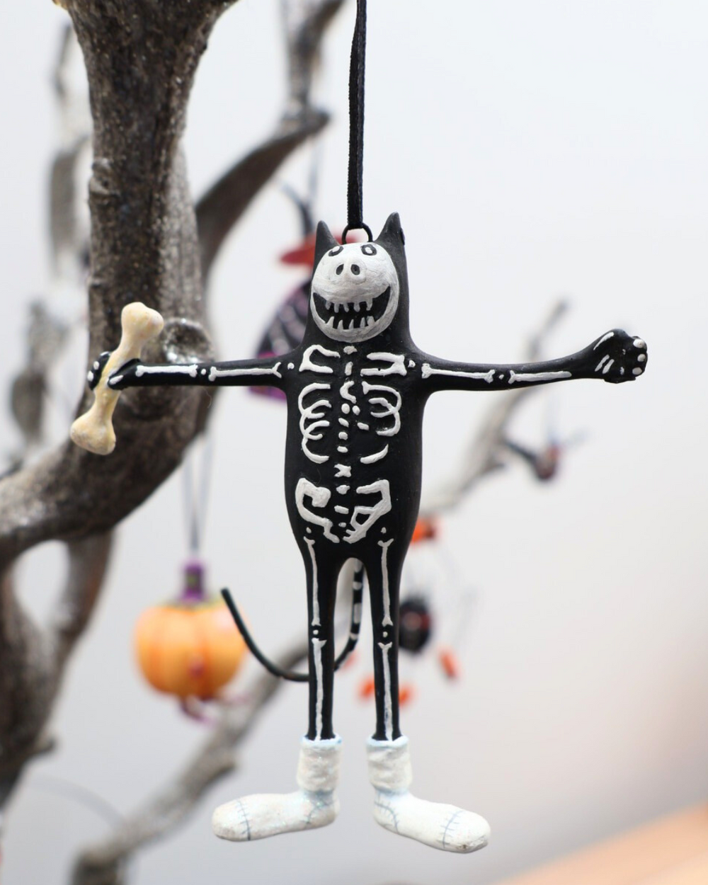 An einem Ast hängende Krinkle Katze Mini Boney Cat als Halloween Dekoration von Patience Brewster.