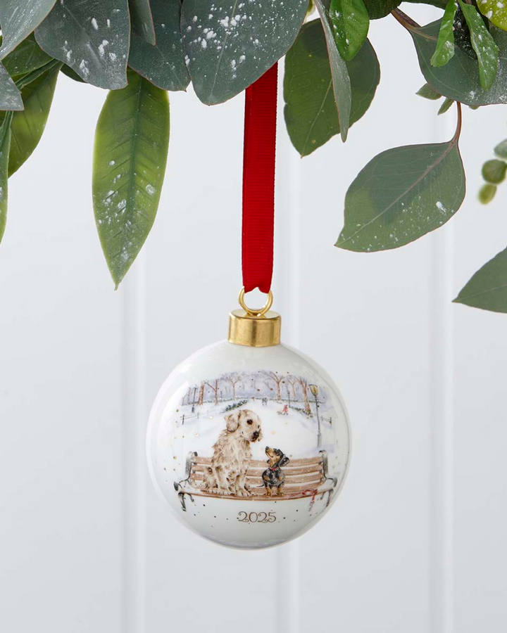 Porzellan Weihnachtskugel 2025 Winter Walks mit Hunden von Wrendale Designs hängend am roten Band.
