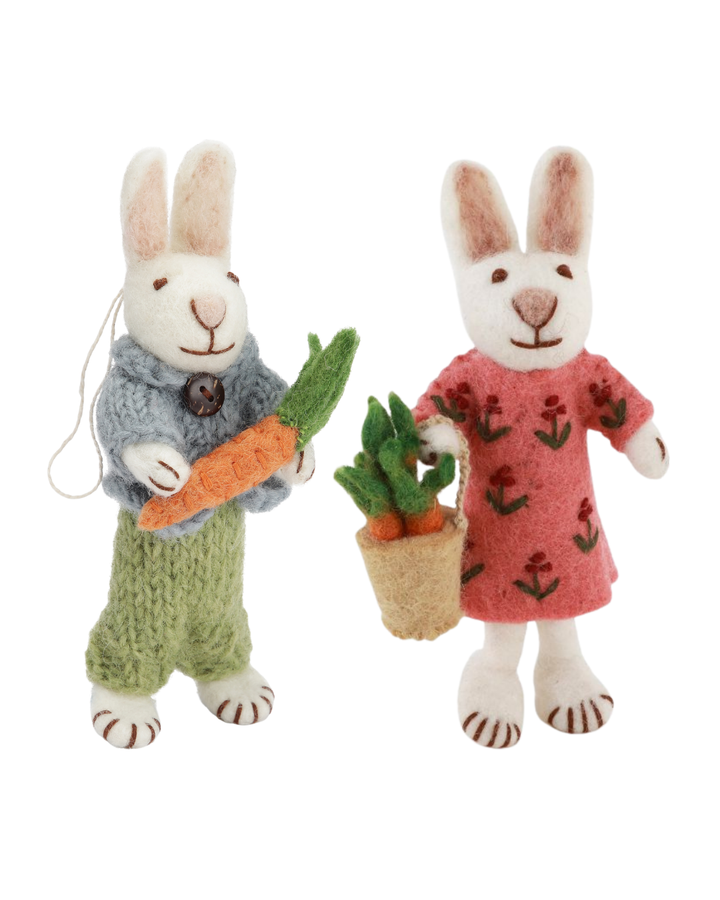 Zwei handgefilzte Hasen als Filzanhänger von Gry & Sif, einer mit blauem Pullover und Karotte, der andere mit rosafarbenem Kleid und Karottenkorb, freigestellt vor weißem Hintergrund.