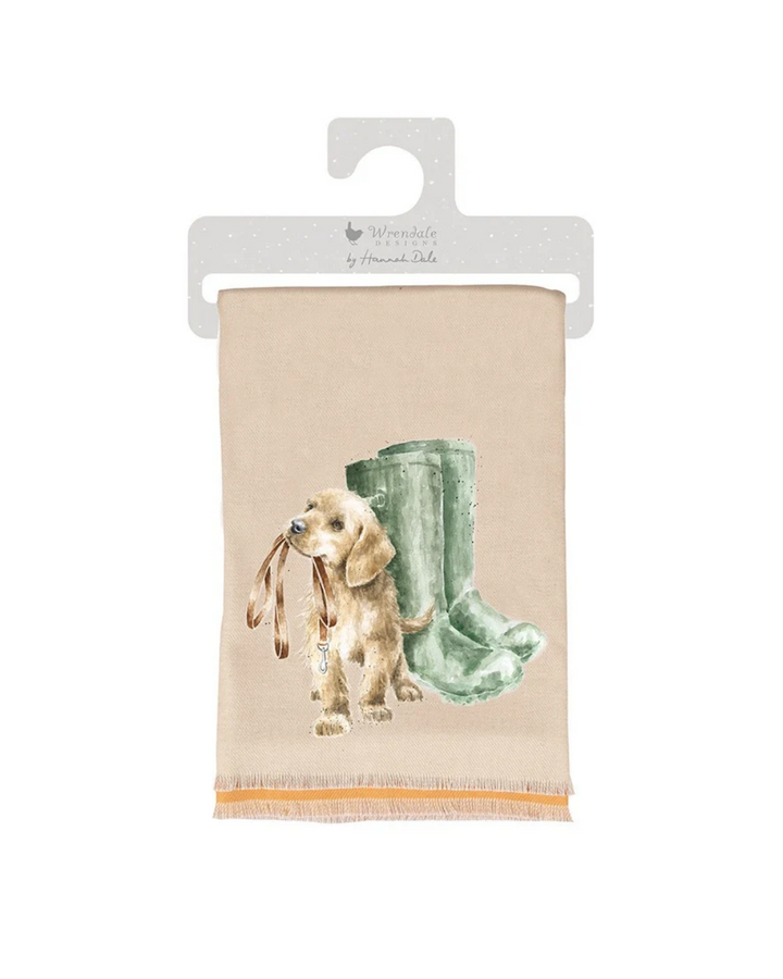 Hunde Schal "Hopeful" von Wrendale Designs vor weißen Hintergrund. Der Schal ist Beige mit einem süßen Hund welcher neben grünen Stiefeln eine Leine im Mund hält.