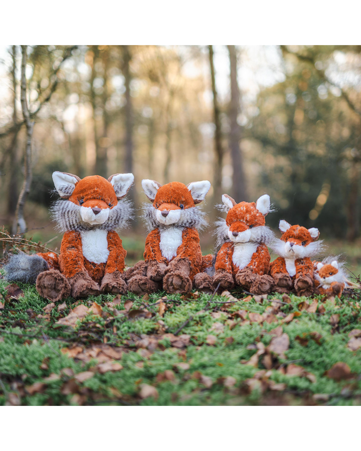 4 Fuchs Kuscheltiere von Wrendale Designs und ein Fuchs Schlüsselanhänger. Die Füchse sitzen in einer Reihe im Wald und sind nach der Größe geordnet.