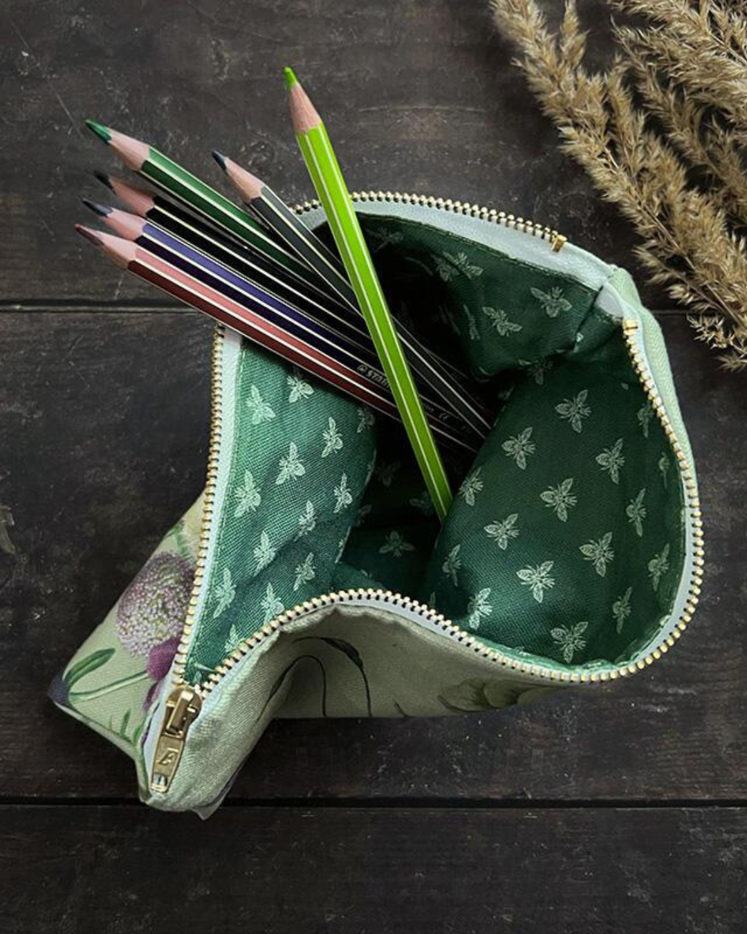 Kosmetiktasche aufrecht stehend mit Blick auf die Knallgrüne Innenseite gefüllt mit bunten Stiften. Die Kosmetiktasche steht auf einem holzigen Tisch