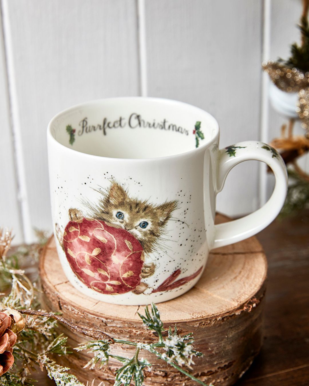 Das Motiv der Katzen Weihnachtstasse von Wrendale Designs zeigt eine Babykatze, die hinter einer Weihnachtsbaumkugel hervorschaut. Im Inneren der Tasse steht "Purrfect Christmas".