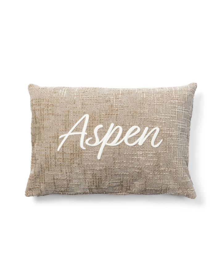 Vorderseite des beigen Kissenbezugs mit weißem „Aspen“-Schriftzug von Rivièra Maison vor weißem Hintergrund.