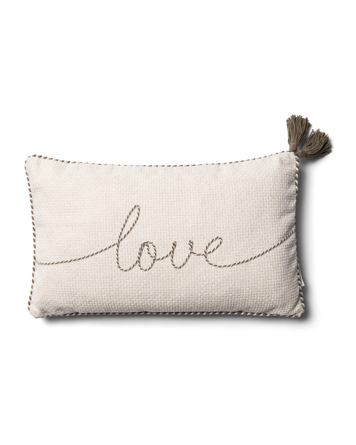 Freigestellter Kissenbezug „With Love Pillow Cover 50x30“ von Rivièra Maison in hellem Naturton mit sichtbarer Struktur, Schriftzug-Stickerei „love“ und Quaste an der Ecke vor weißem Hintergrund.