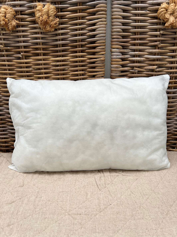 Eine rechteckige 45 x 65 cm Kissenfüllung von Rivièra Maison liegt auf einer braunen Decke vor einem Paravant aus Rattan.