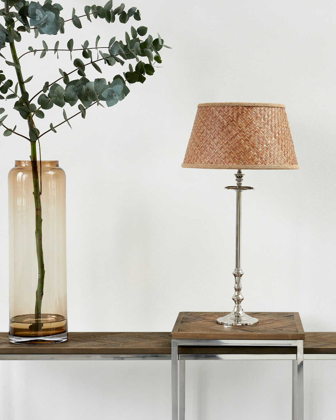 Lampenfuß L'Hotel Lampbase von Rivièra Maison mit geflochtenem Lampenschirm auf Holzkonsole, neben transparenter Glasvase mit Zweigen vor heller Wand.