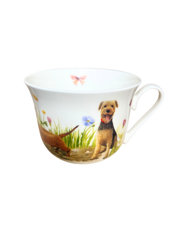 Porzellantasse „Hundespaß“ vom Grätz Verlag mit Illustrationen von Maria Over, zeigt zwei Hunde in einer bunten Blumenwiese mit flatterndem Schmetterling vor weißem Hintergrund.