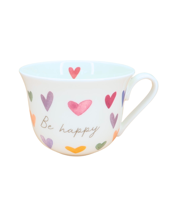 Weiße Keramik-Tasse mit bunten Herzen und der Aufschrift „Be happy“ der Marke Grätz Verlag, isoliert auf weißem Hintergrund.