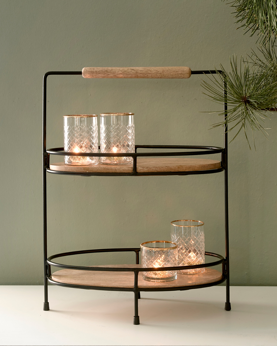 Die Lower East Side Etagere von Rivièra Maison ist mit vier Glas Windlichtern auf einer weißen Kommode vor einer mintgrüner Wand dekoriert.