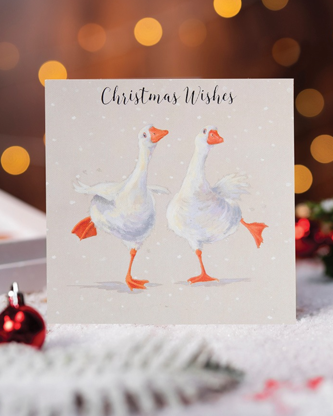 Luxuriöses Gänse Weihnachtskartenset von Wrendale Designs mit 8 Karten und pssenden Umschlägen. Illustriert von Hannah Dale. Zu sehen ist eine einzelne Karte vor weihnachtlicher Beleuchtung.