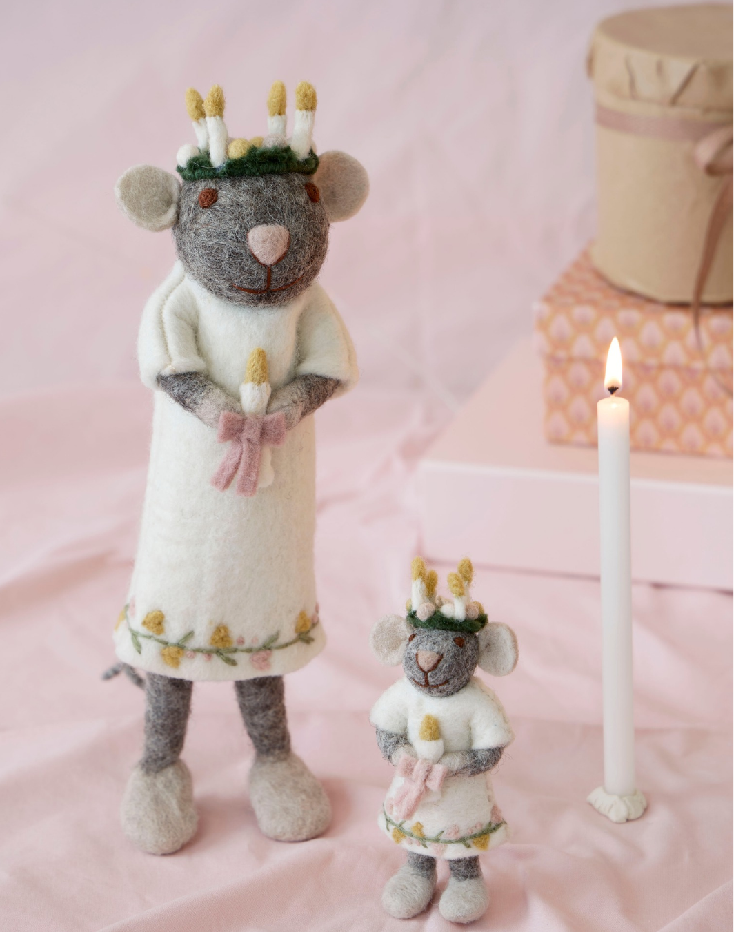 Heilige Mäuse Mädchen "Lucia" von Gry & Sif dekoriert. Zu sehen sind 2 graue Mäuse eine größere und eine kleinere mit einem weißen Oberteil und einer pinken schleife mit einer Kerze in den Händen. Sie tragen ein Kranz mit vielen Kerzen auf dem Kopf.  Im Hintergrund ist eine Kerze und Geschenkverpackungen zu sehen.