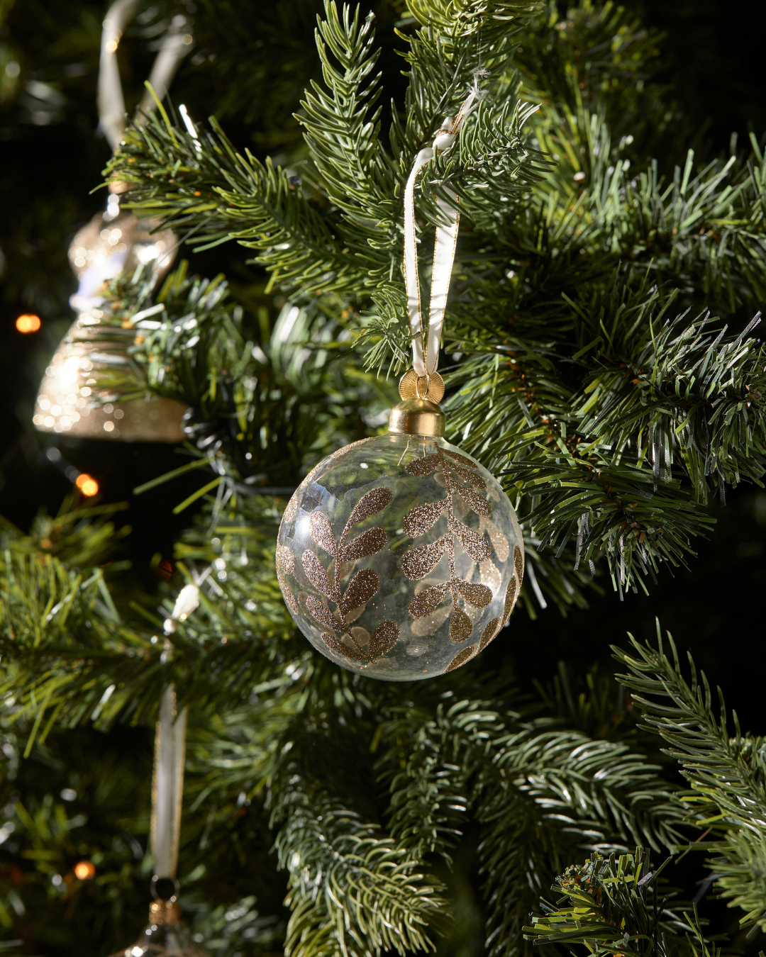 Weihnachtsbaumkugel „Magic Mistletoe“ von Rivièra Maison am Tannenbaum mit goldenen Mistelzweigen auf transparentem Glas.