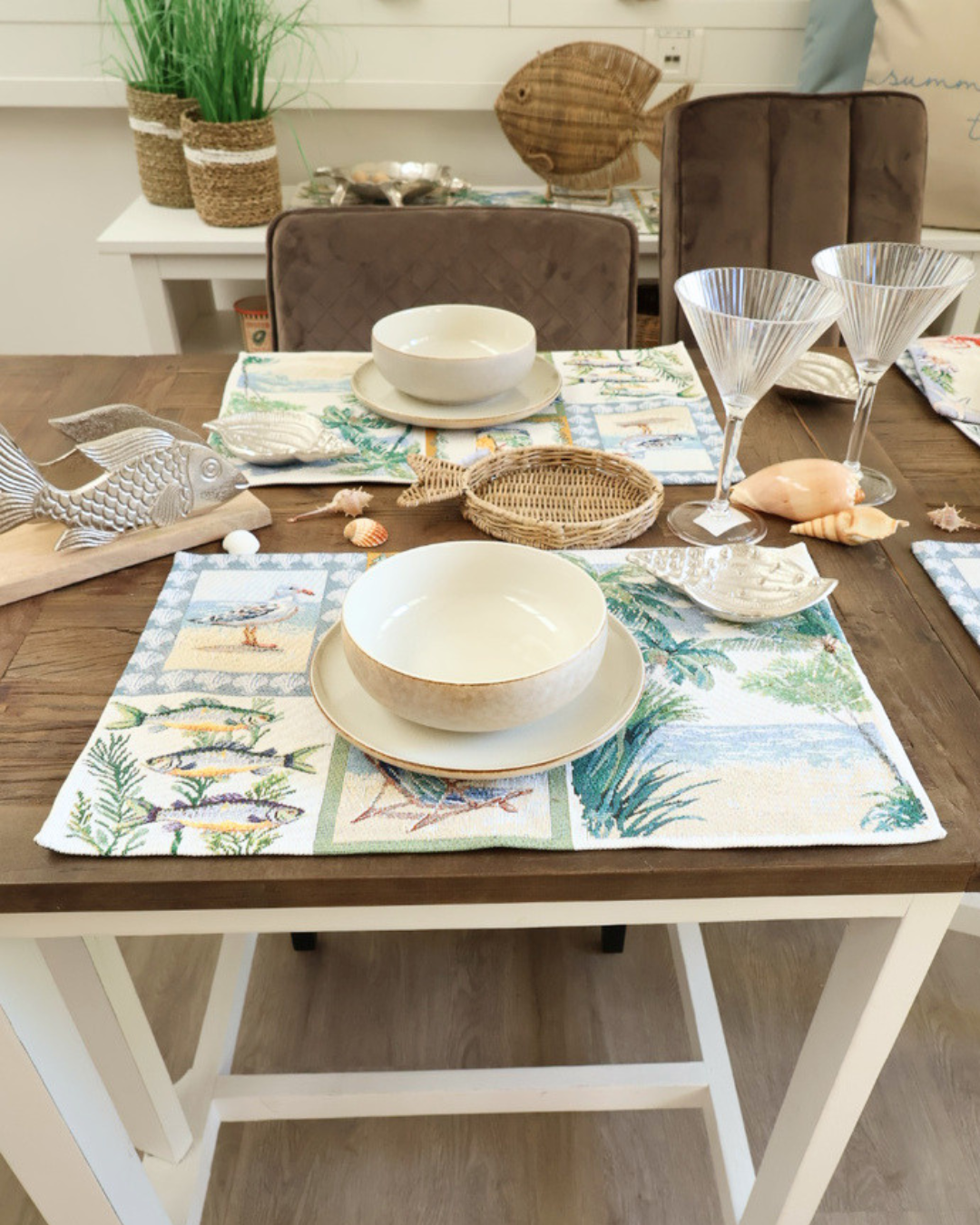 Maritim dekorierter Frühstückstisch mit "Costa" Platzsets von Sander und weißen Schüsseln von Riviera Maison. Der Tisch ist braun und mit schicken gläsern Muscheln etc. dekoriert.