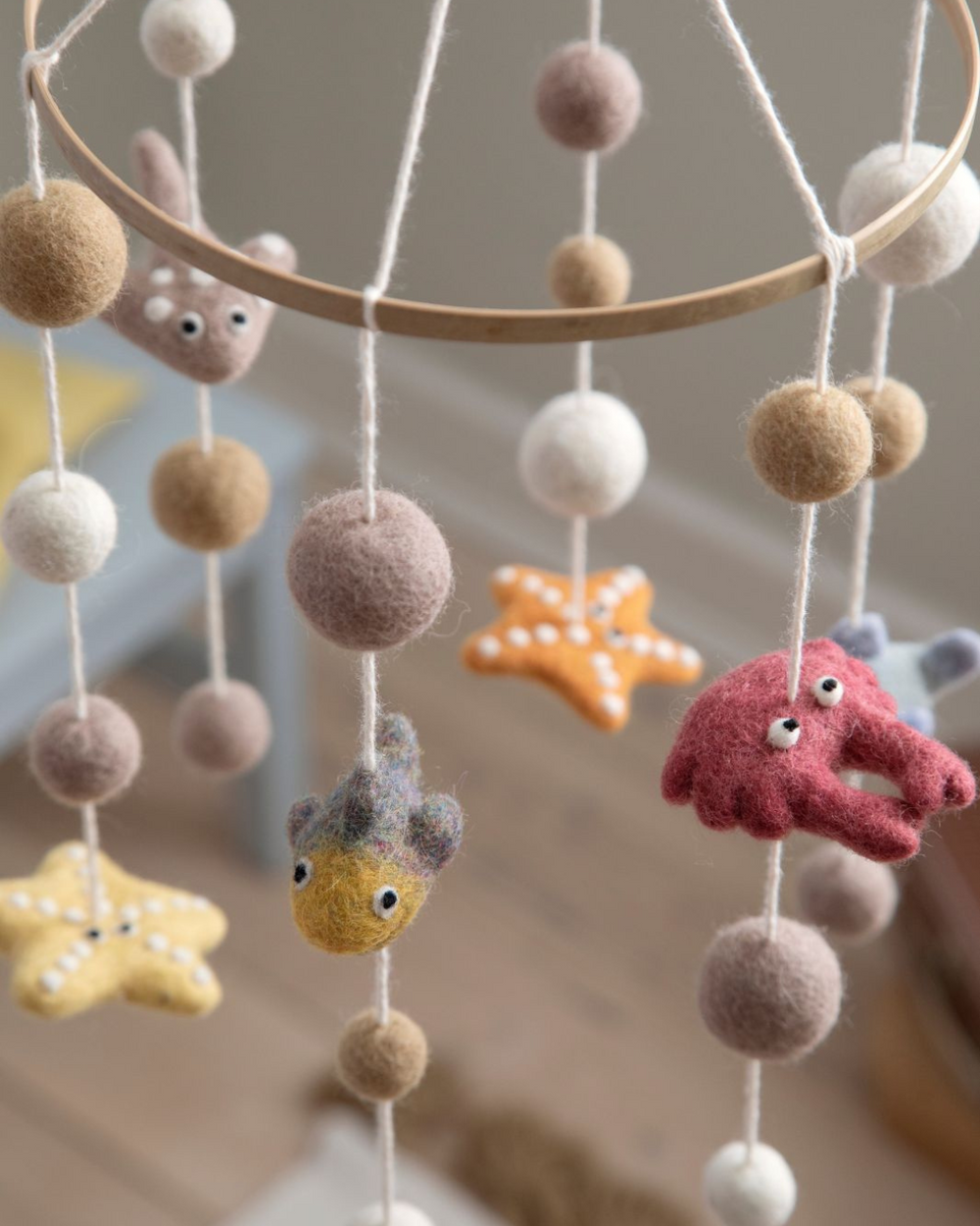 Mobile mit Meerestieren aus Filz hängt vor unscharfem Hintergrund im Kinderzimmer.