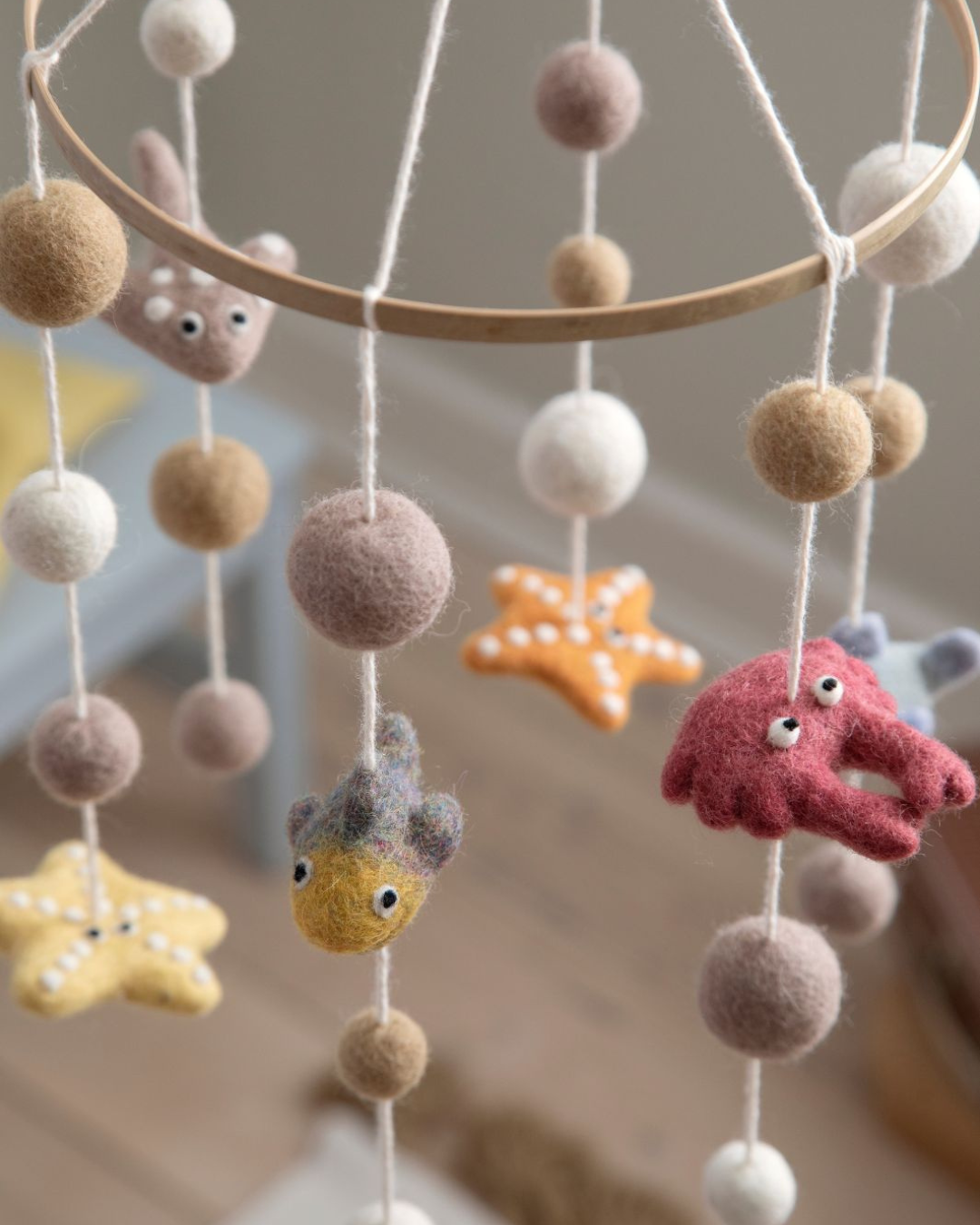 Mobile mit Meerestieren aus Filz hängt vor unscharfem Hintergrund im Kinderzimmer.