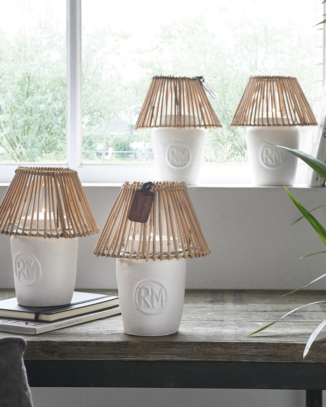 Mehrere Windlichter „RM Clay Candle Holder“ von Rivièra Maison mit Kerzen auf einer Fensterbank arrangiert.