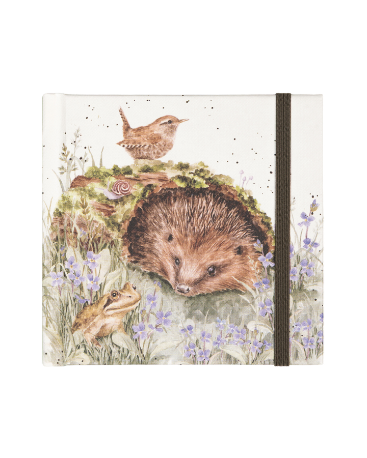 Die Vorderseite des Mini Notizbuchs The Wild Patch von Wrendale Designs zeigt einen Igel, der unter einer Moosbewachsenen Baumstammrinde hervorschaut. Auf der Rinde sitzt ein kleiner Vogel und in der Wiese sitzt ein freundlich blickender Frosch. Mit detailliertem Design von Hannah Dale. 
