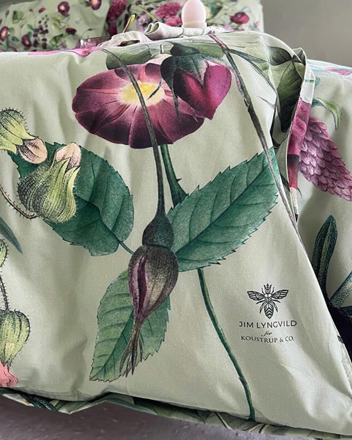 Kissenbezüge Blossom Garden mit Blumenmotiven in Rosa, Lila und Grün, gestapelt auf einem Bett.
