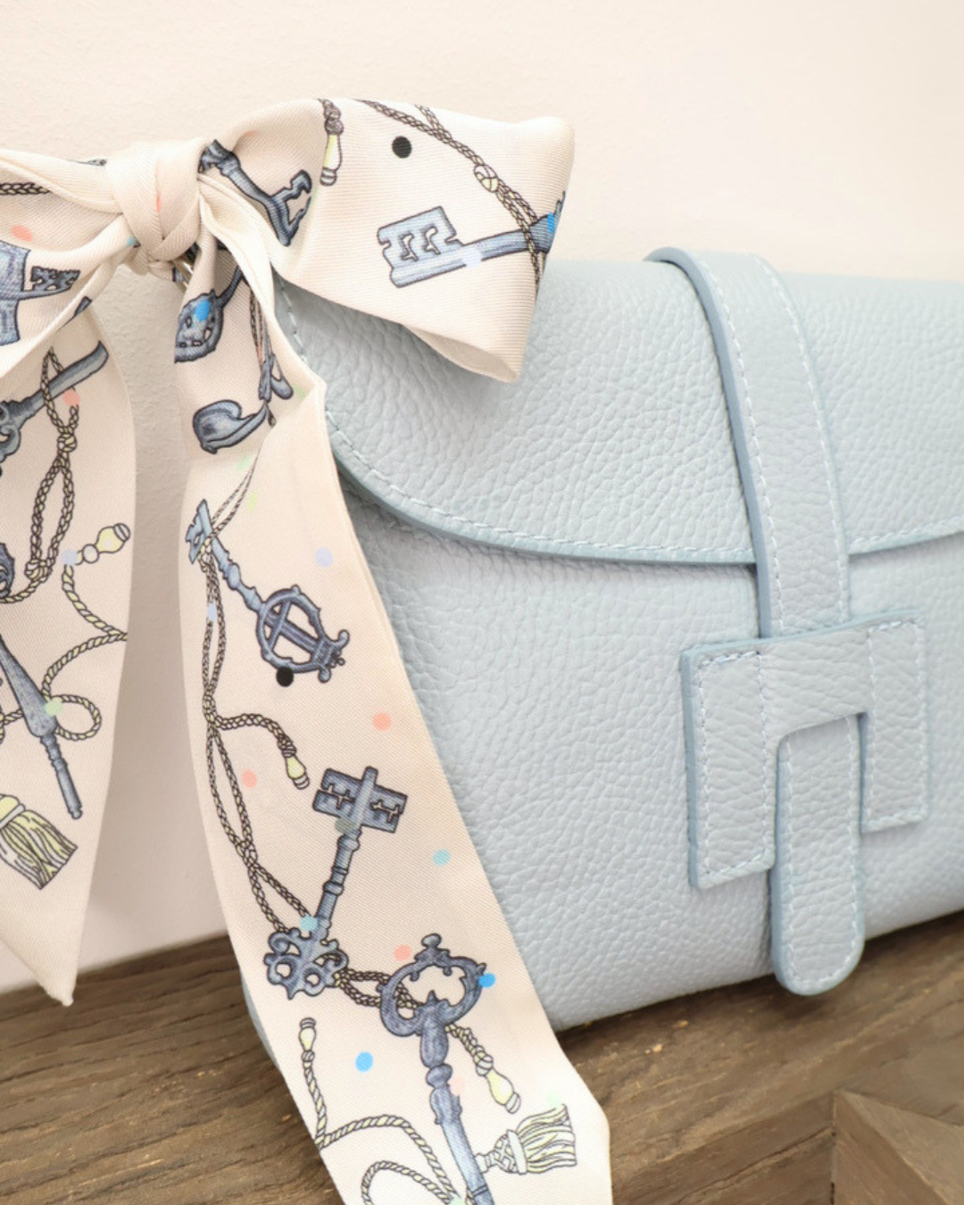 Nahansicht der Ledertasche "Isabella" vom Südstrand in Hellblau. Die Tasche liegt auf einem Holztisch vor einem weißen Hintergrund während das kunstvolle bläuliche-Bandana gut zu sehen ist.