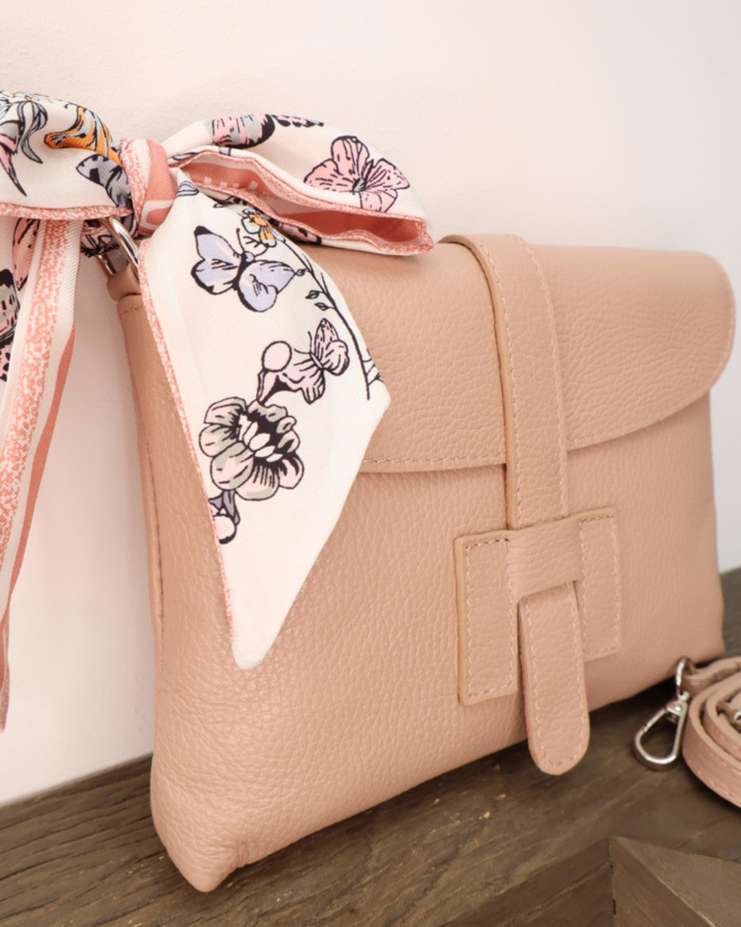 Nahansicht der Ledertasche "Isabella" vom Südstrand in der Farbe Puder. Die Tasche liegt auf einem Holztisch vor einem weißen Hintergrund während das helle florale-Bandana gut zu sehen ist.