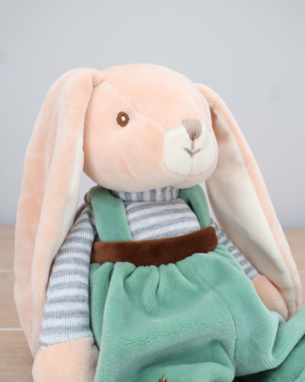 Ein Hase mit mintfarbenem Overall und braunem Latz von Bukowski sitzt auf einem Holzboden.