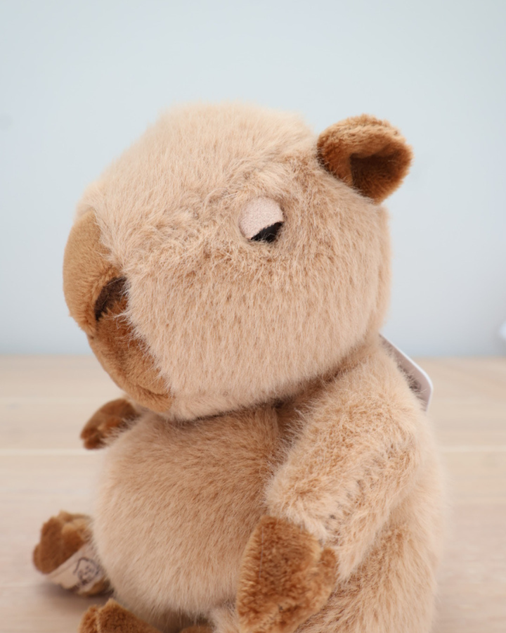 Ein Capybara von Bukowski sitzt auf einem hellen Holztisch. Die braunen Pfoten und Ohren sind gut zu erkennen.