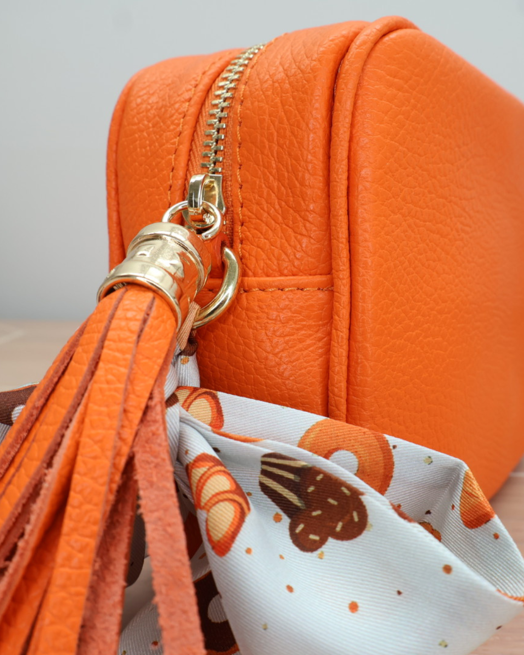 Nahaufnahme des Reißverschlusses der orangen Lederhandtasche „Isolde“ mit Bandana-Anhänger in Tieroptik.
