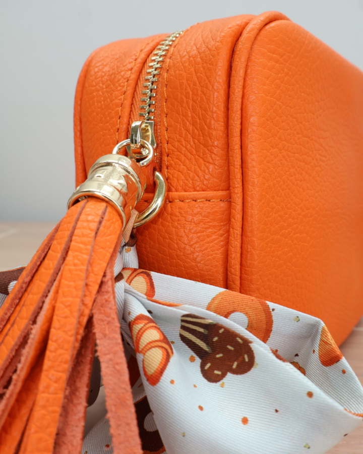 Nahaufnahme des Reißverschlusses der orangen Lederhandtasche „Isolde“ mit Bandana-Anhänger in Tieroptik.
