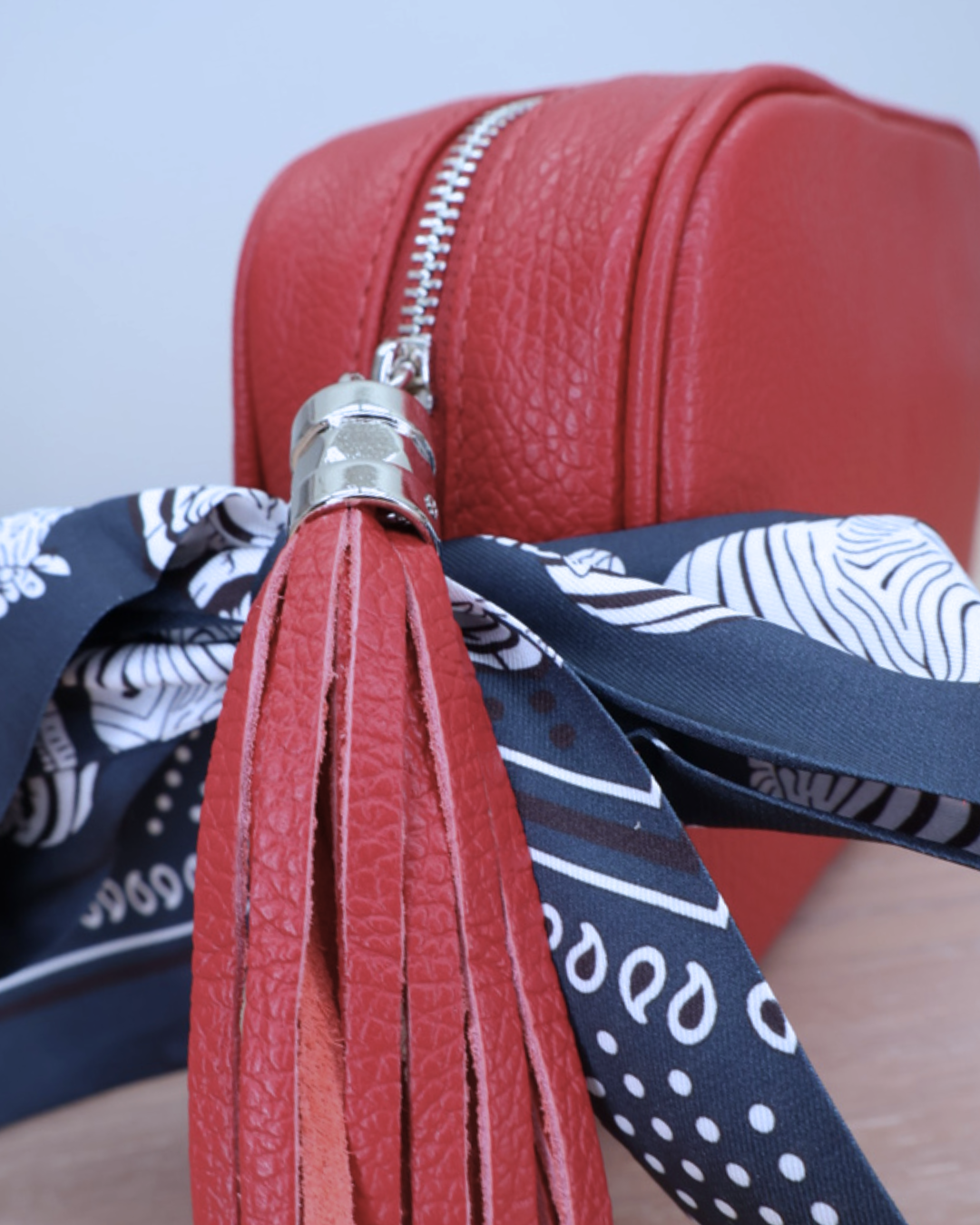 Nahaufnahme des Reißverschlusses der roten Lederhandtasche „Isolde“ mit Bandana-Anhänger.