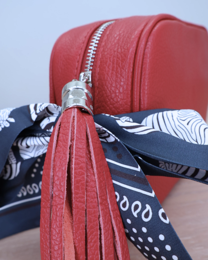 Nahaufnahme des Reißverschlusses der roten Lederhandtasche „Isolde“ mit Bandana-Anhänger.