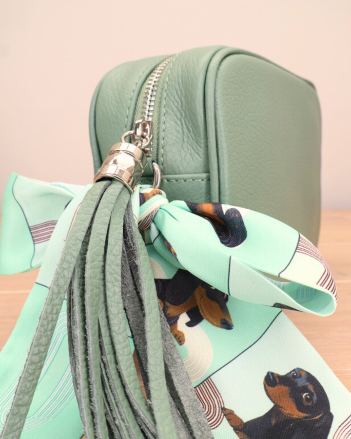 Nahaufnahme des Reißverschlusses der grünen Seegras Lederhandtasche „Isolde“ mit Bandana-Anhänger und goldfarbenem Metallverschluss.