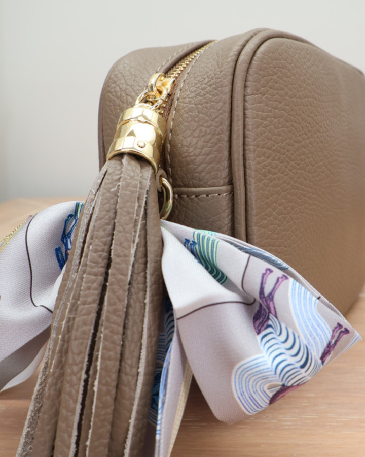 Nahaufnahme des Reißverschlusses der Taupen Lederhandtasche „Isolde“ mit Bandana-Anhänger.