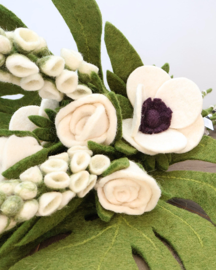 Detailaufnahme des Hochzeits-Blumenstraußes aus Filz mit natürlichen Akzenten wie Fingerhut, Monstera-Blättern, Rosen, Anemonen und Palmblättern in cremigen und zartrosa Tönen.