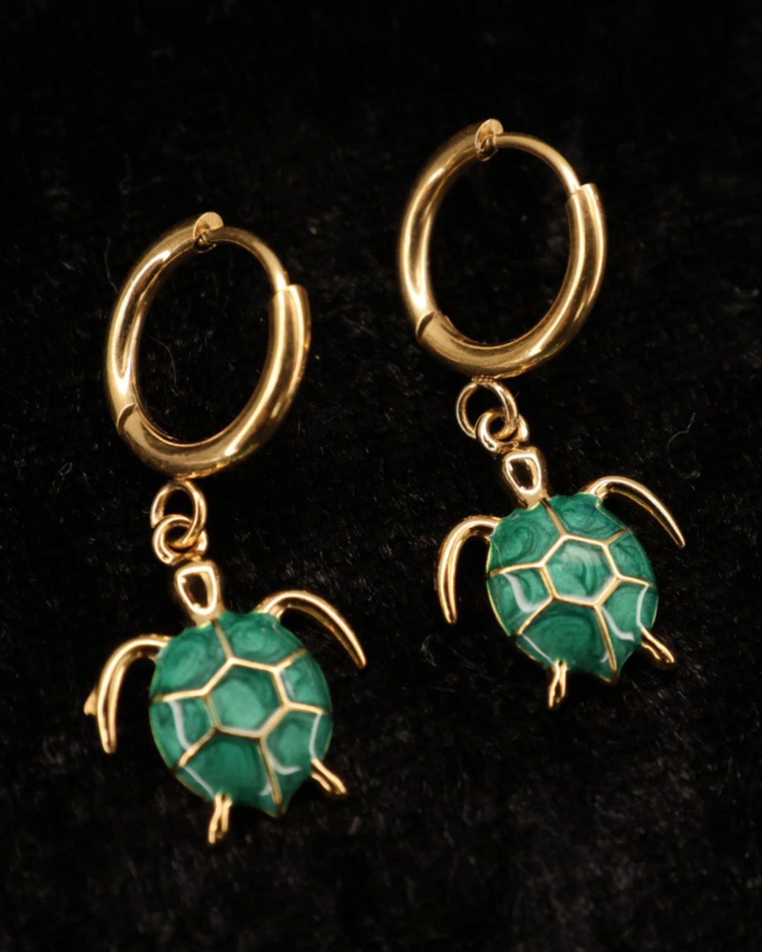 Goldene grüne Emaille-Schildkröten Ohrringe von Dottilove auf schwarzer leicht glitzernder Decke.