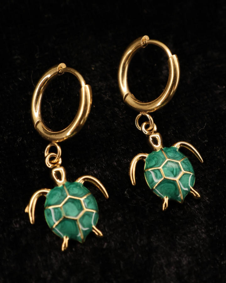 Goldene grüne Emaille-Schildkröten Ohrringe von Dottilove auf schwarzer leicht glitzernder Decke.
