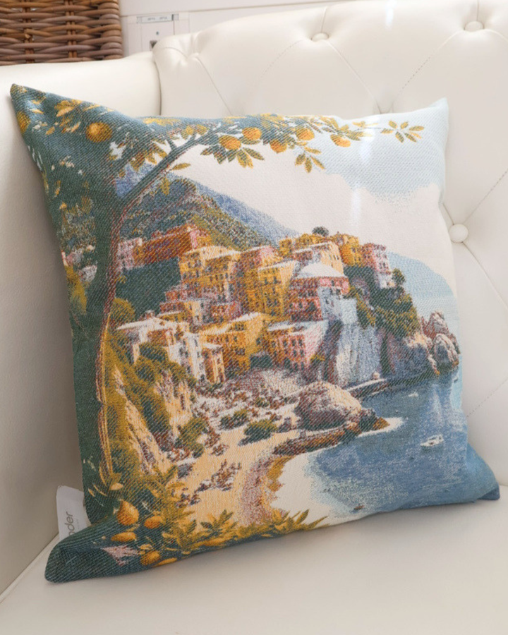 Nahaufnahme des "Positano" von Sander. Das Motiv besteht aus einer schönen farbvollen Küste und einem Zitronenbaum im Vordergrund. Das Kissen liegt auf einem weißen Sofa.