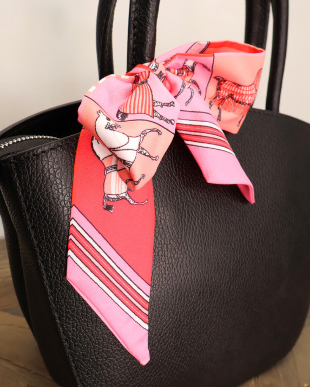 Schwarze Handtasche aus Leder Lotte vom Südstrand mit pinken Bandana auf hellen Holztisch vor weißen Hintergrund.