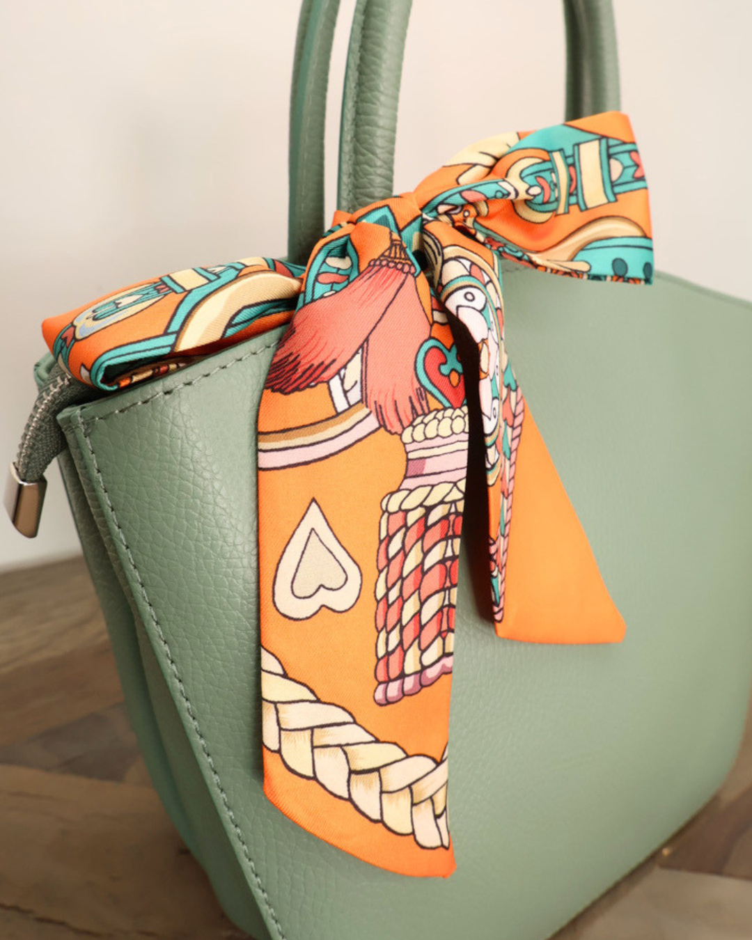 Seegrüne Handtasche aus Leder Lotte vom Südstrand mit orangenem Bandana auf hellen Holztisch vor weißen Hintergrund.