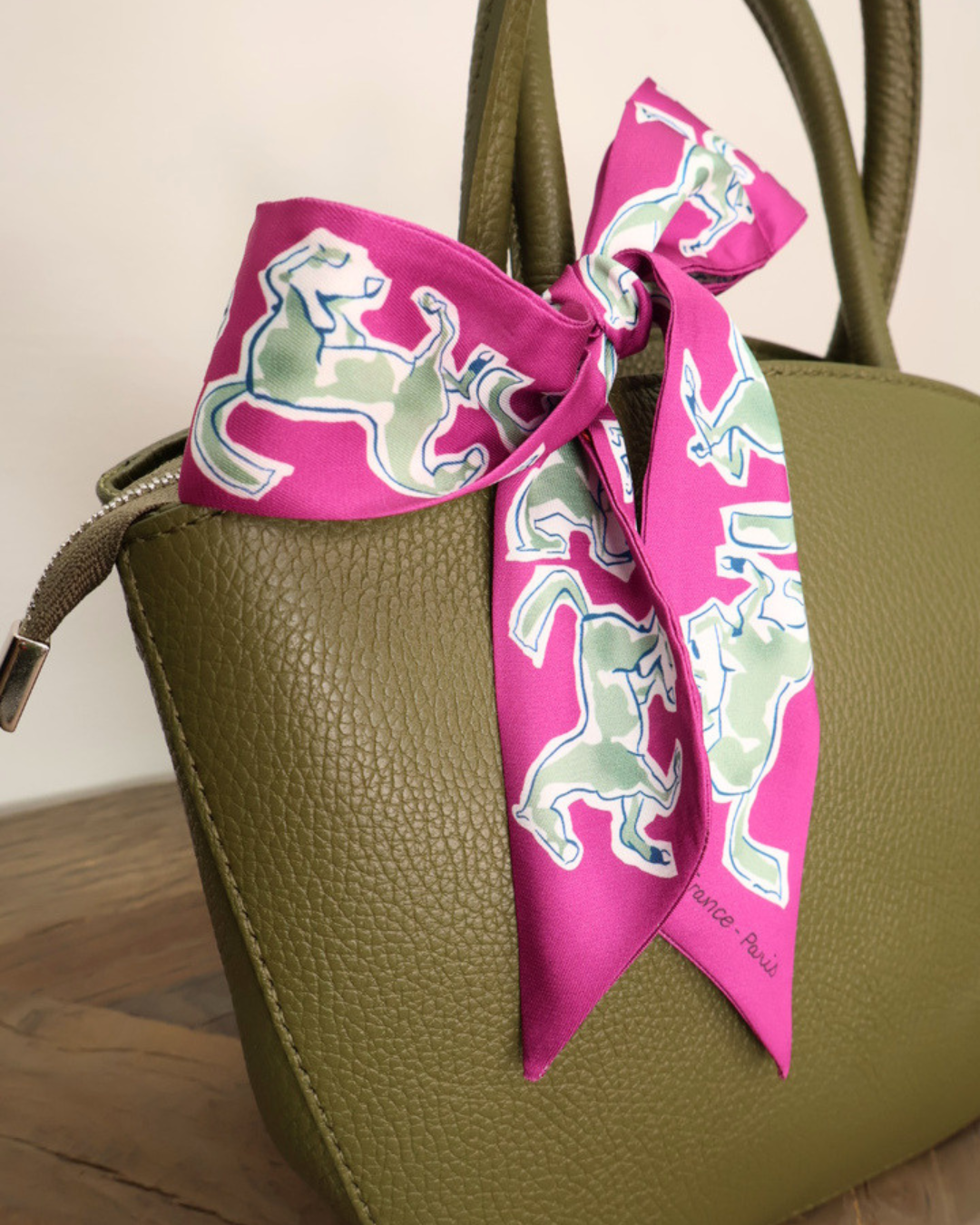 Waldgrüne Handtasche aus Leder Lotte vom Südstrand mit pinken Bandana auf hellen Holztisch vor weißen Hintergrund.