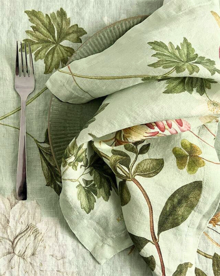 Leinenserviette "Flora Danica Atlas" von Koustrup & Co., locker gefaltet neben Gabel auf Tischdecke mit botanischen Motiven.