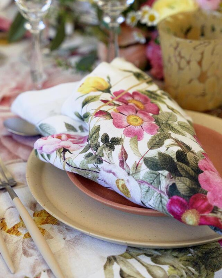 Leinenserviette "Rose Flower Garden" von Koustrup & Co., gefaltet auf Teller mit Besteck und Gläsern auf festlich gedecktem Tisch.