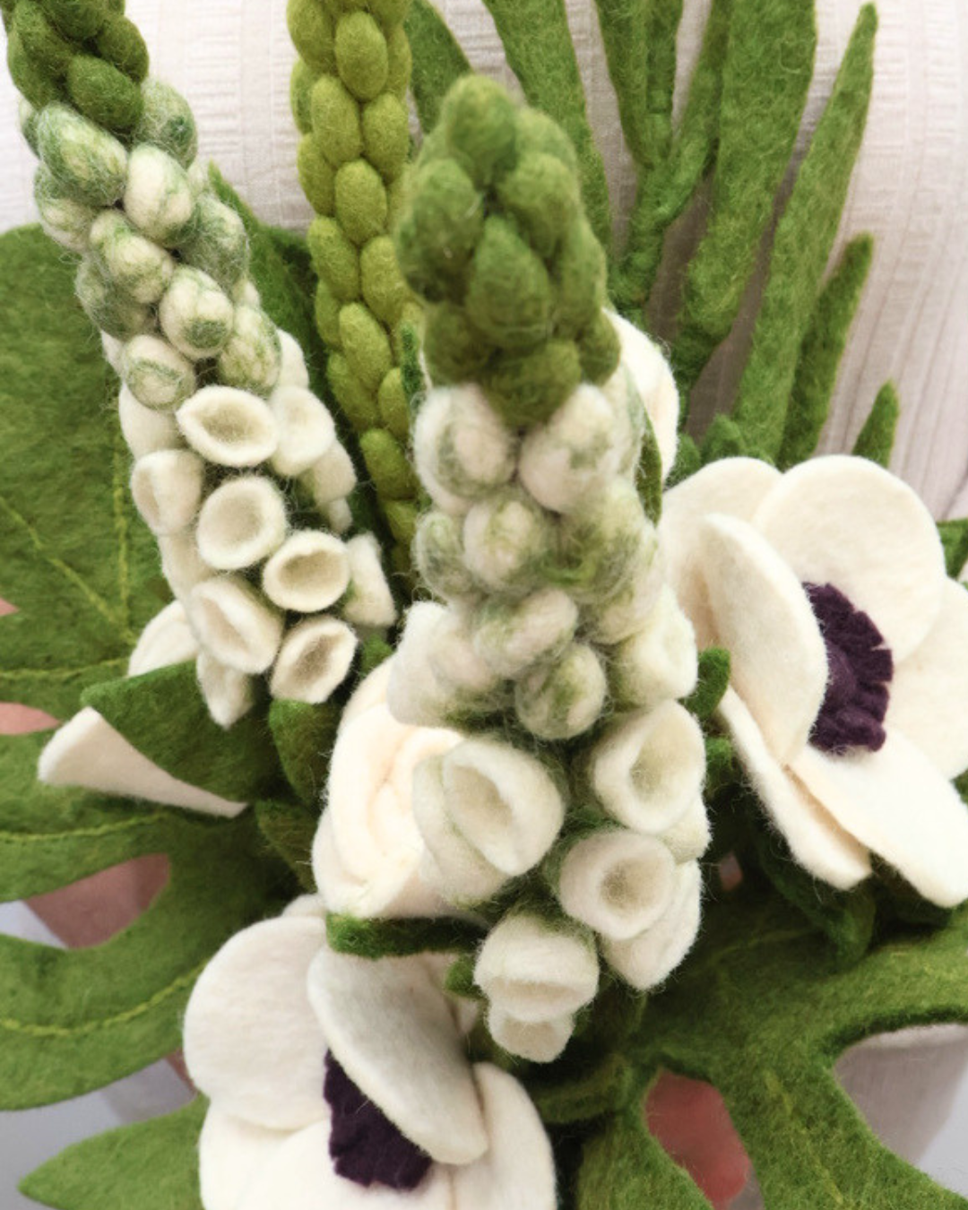 Detailaufnahme des Hochzeits-Blumenstraußes aus Filz mit natürlichen Akzenten wie Fingerhut, Monstera-Blättern, Rosen, Anemonen und Palmblättern in cremigen und zartrosa Tönen.