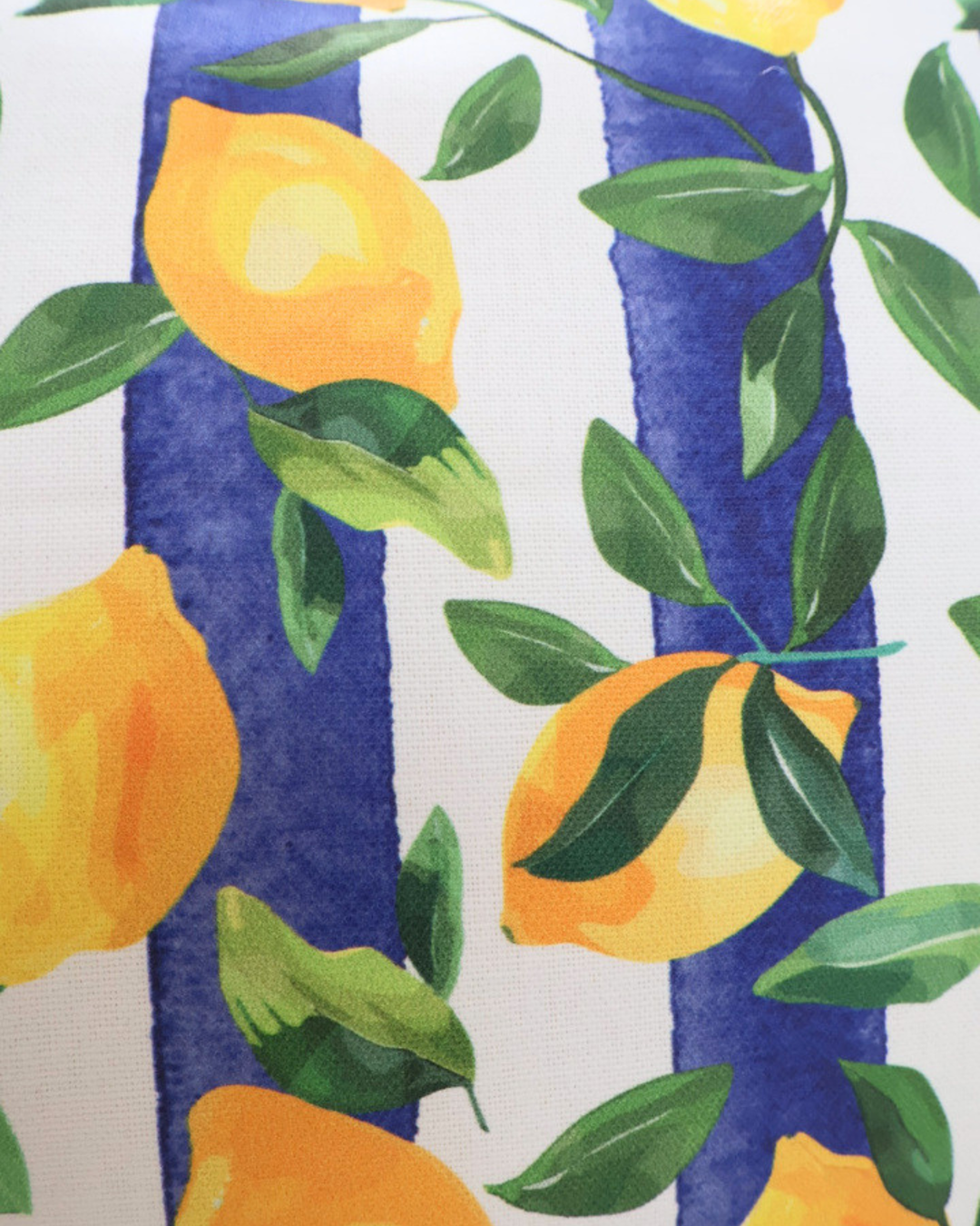Nahaufnahme des Zitronen Kissens "Lemontree". Das Motiv besteht aus Blättern und Zitronen vor einem Blau Weiß gestreiften Hintergrund. Die Details sind gut erkennbar.