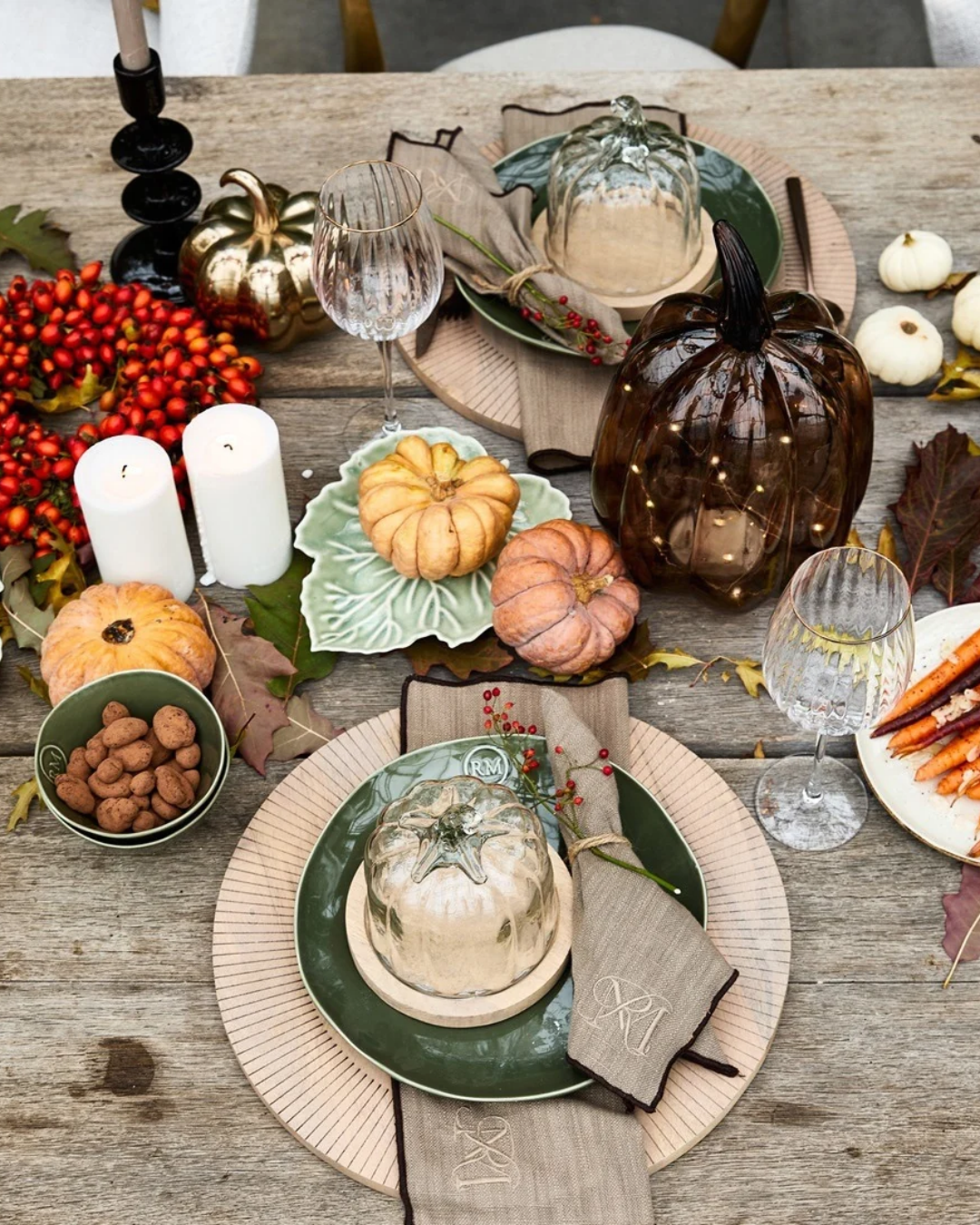 Zwei Kürbis Glasglocken "Pumpkin Cloche" von Riviera Maison mit Holzuntersetzer mit schwarzer RM Aufschrift. Auf diesem Bild auf einem gedeckten Tisch stehend.