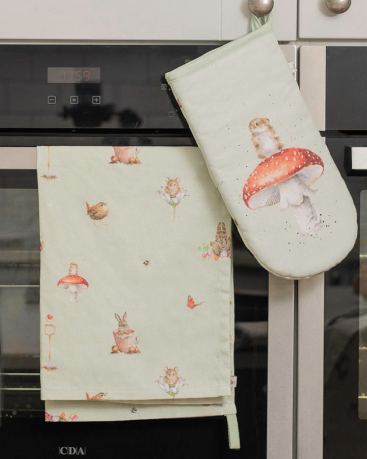 Ein Ofenhandschuh mit der Maus auf dem Fliegenpilz und ein passendes Geschirrtuch mit den Gartentieren von Wrendale Designs drauf, hängen an einem Backofen.