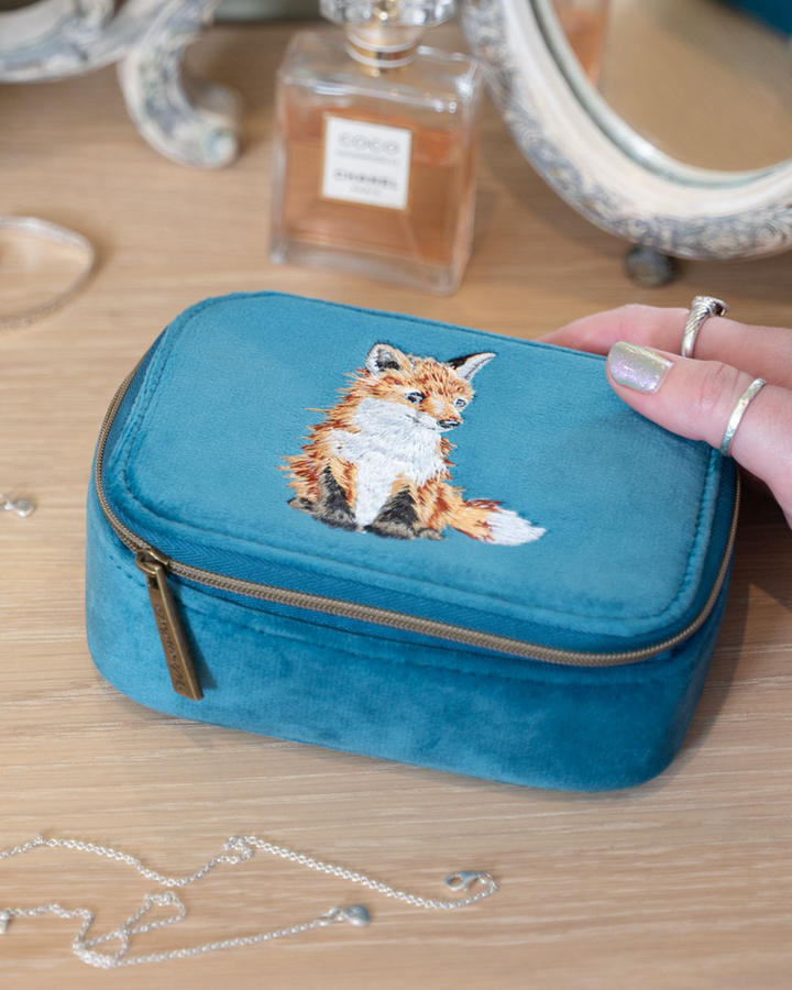 Petrolfarbene Schmucktasche mit Fuchsmotiv von Wrendale Designs auf einem Schminktisch neben einem Parfumflakon.